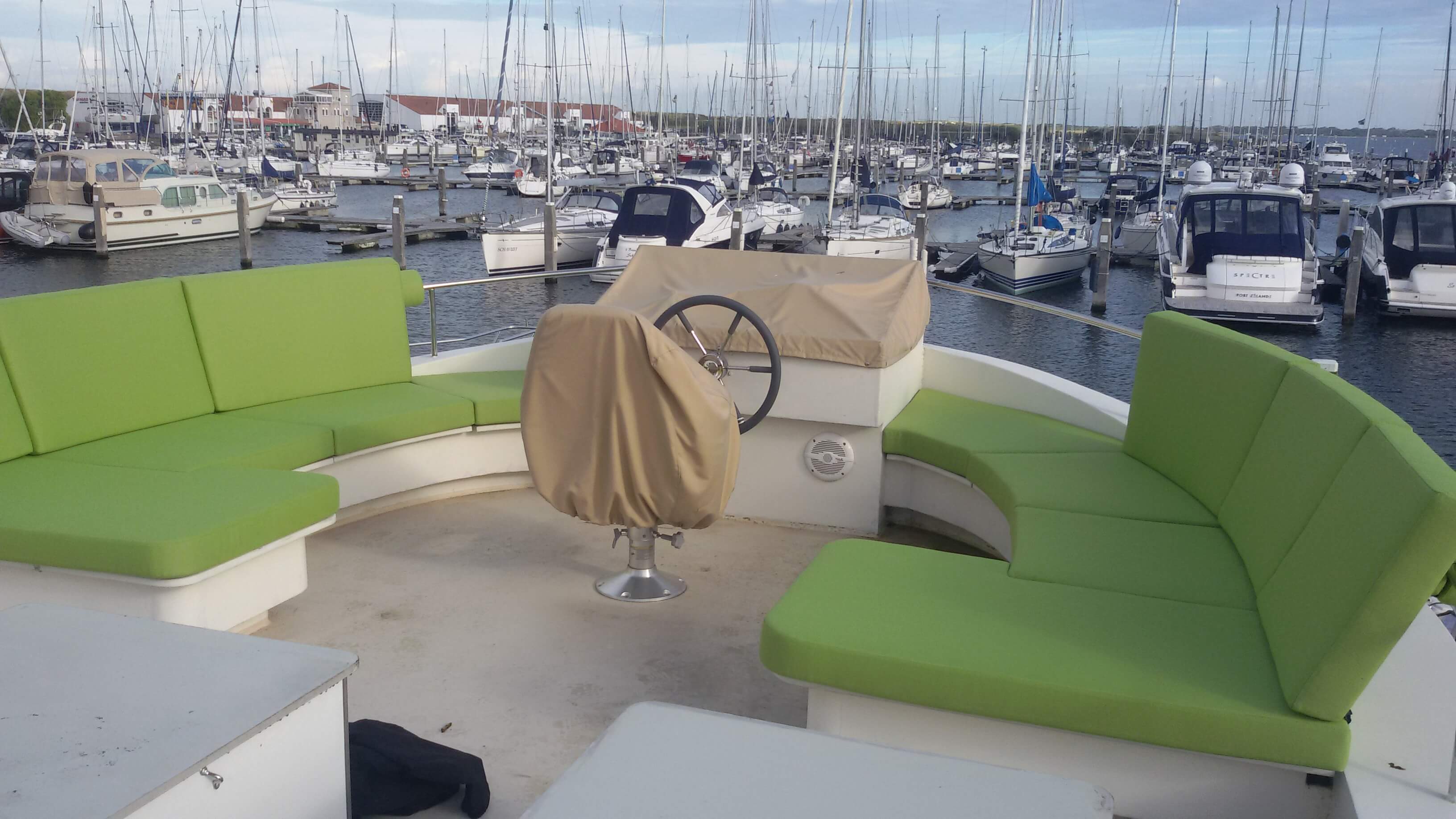 Flybridge van een motorjacht met felgroene maatwerkkussens in een jachthaven